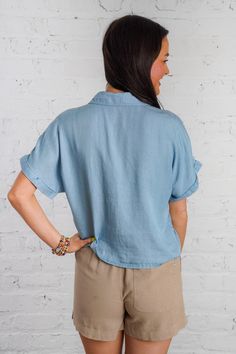 Ride the waves of style with our Drifting Tides Top. This blue chambray top features a button down front, a tie detail, and a front pocket, perfect for a casual yet chic look. The short cuffed drop sleeves and collared neckline add a touch of charm, while the soft chambray material provides ultimate comfort. Pair with our Sand Dune Shorts and Sunbeam Raffia Mules to complete the look! This top is lightweight, non-sheer, and has a loose boxy fit. 100% Tencel Brand- Be Cool Model is 5'5" and is we Washed Blue Chambray Button-up Top, Casual Blue Top With Rolled Sleeves, Casual Blue Tops With Rolled Sleeves, Blue Collared Top With Roll-up Sleeves, Blue Casual Tops With Cuffed Sleeves, Linen Tops With Roll-up Sleeves, Casual Blue Tops With Cuffed Sleeves, Casual Chambray Button-up Blouse, Washed Blue Summer Top With Pockets