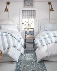 two beds in a bedroom with blue and white bedding, rugs and lamps