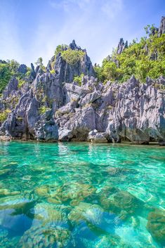 the water is crystal blue and clear with rocks on either side, and green trees in the background