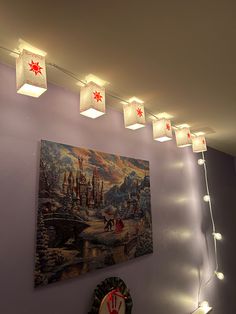 some lights are hanging on the wall above a painting