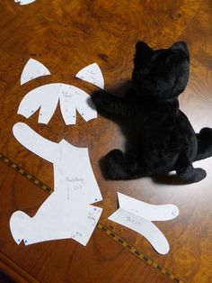 a black teddy bear sitting on top of a wooden table next to cut out pieces of paper