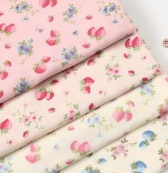 three pieces of pink fabric with strawberrys and blue flowers on the bottom, one is white