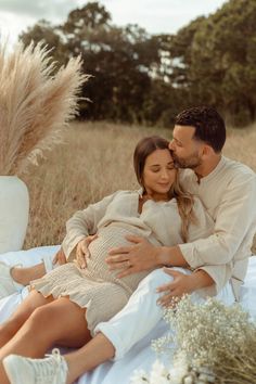 a man and woman cuddle while sitting on a blanket in a field with tall grass