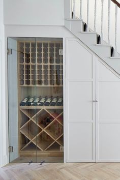 a wine cellar under the stairs in a house with wood floors and white walls,