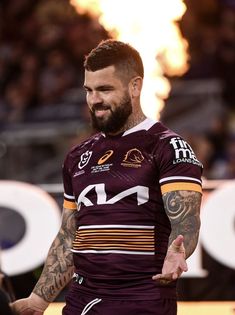 a man with a beard wearing a maroon and gold rugby jersey standing in front of a crowd