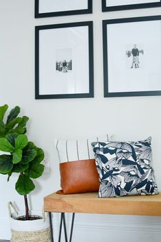 a wooden bench topped with pillows next to pictures on the wall and a potted plant