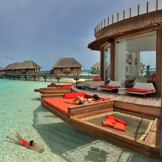 people are lounging in the water near lounge chairs and thatched huts on the beach