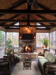 an outdoor living room with couches, tables and a television on the fireplace screen