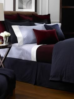 a bed with red and blue sheets in a bedroom next to a night stand on a wooden floor