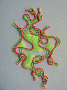 a piece of art made out of neon colored thread and plastic beads on a gray surface