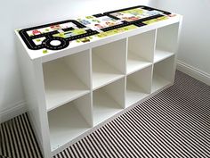 a white book shelf with black and white tiles on it's top, next to a striped floor