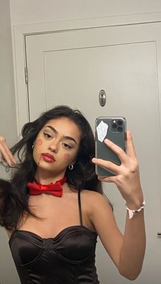 a woman taking a selfie in front of a mirror wearing a red bow tie