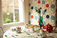 a table with plates and cups on it in front of a wallpapered window