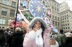 a woman is standing in the middle of a crowded street with an astronomical clock behind her