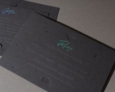 two black business cards with green and blue ink on them