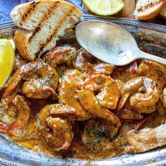 a bowl filled with shrimp and bread on top of a blue table cloth next to lemon wedges