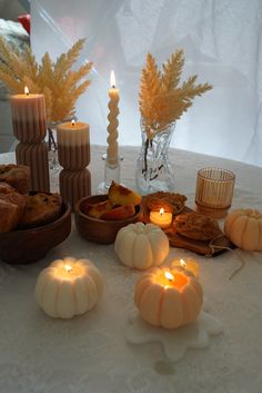 a table topped with candles and pumpkins on top of a white tablecloth covered table