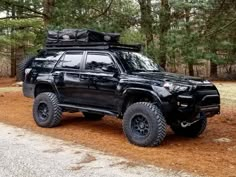 a black truck parked on the side of a dirt road in front of some trees