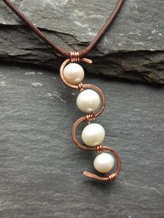 a necklace with three pearls hanging from it's end on a stone surface next to a rock