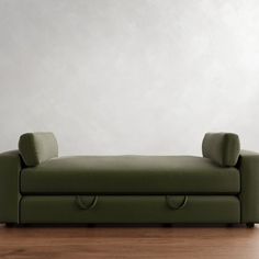 a green couch sitting on top of a hard wood floor next to a white wall