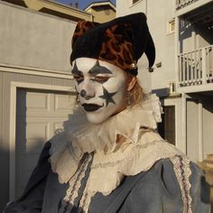 a man with painted face and nose is standing in front of a building wearing a costume