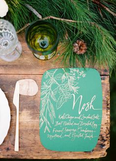 a wooden table topped with plates and utensils next to a pine tree branch