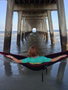 a woman laying in a hammock on the beach with her arms spread out