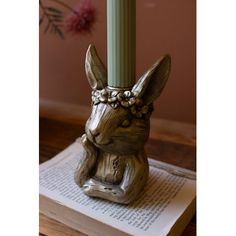 a wooden rabbit figurine sitting on top of an open book next to a candle