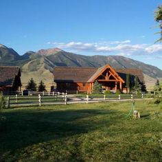 a large wooden house sitting in the middle of a lush green field next to mountains