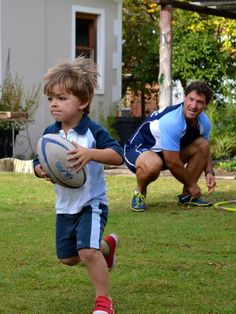 a young boy running with a frisbee in his hand while another man crouches behind him