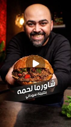 a man holding up a large sandwich with meat and veggies on it in front of him