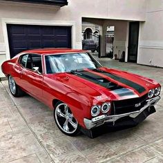 a red and black muscle car parked in front of a garage with its hood up