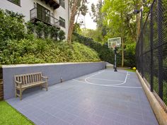 an outdoor basketball court surrounded by trees and bushes with a bench in the foreground