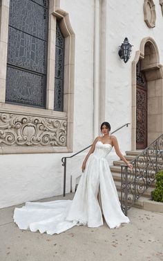 a woman in a wedding dress standing on the steps of a building with her hand on her hip