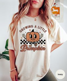 Announce and celebrate your growing family this Thanksgiving with this cute retro "Growing A Little Pumpkin" tee. This is a unisex Comfort Colors T-shirt. ✅ SIZE AND COLORS - For size information and available colors, be sure to check out our sizing and color chart in the photos. - If you are looking for an oversized or looser fit, size up 1-2 sizes. - If you are looking for a "T-shirt dress" look, we recommend sizing up 2 sizes. ✅ KEY FEATURES - Unisex Comfort Colors T-shirt. - Soft-washed and Cute Fall T-shirt For Gift, Retro Short Sleeve Tops As Gift, Fall Crew Neck Birthday T-shirt, Crew Neck Birthday T-shirt For Fall, Retro Short Sleeve T-shirt As A Gift, Retro Crew Neck T-shirt As Gift, Retro Short Sleeve T-shirt For Gifts, Retro Short Sleeve T-shirt As Gift, Retro Funny Print T-shirt As Gift