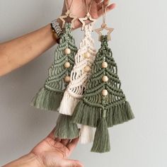 two hands are holding small christmas trees made from yarn and wood beads, one is green and the other is white