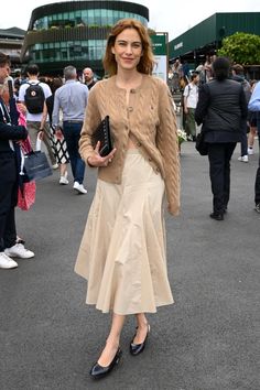 a woman is standing in the middle of a crowd wearing a skirt and cardigan