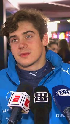 a young man in a blue jacket is holding microphones and talking to the media