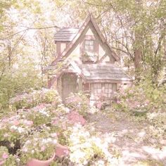 a small house in the middle of some trees and bushes with pink flowers around it