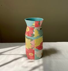 a colorful vase sitting on top of a table next to a white sheet covered wall