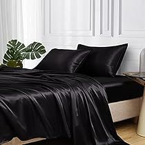 a bed with black sheets and pillows in a white room next to a plant on the floor