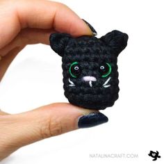 a hand holding a small black cat with green eyes and fangs on it's face