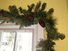 pine cones and evergreen needles are hanging on the window sill in front of a yellow wall