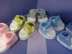 several pairs of crocheted baby shoes are arranged on a purple and blue background