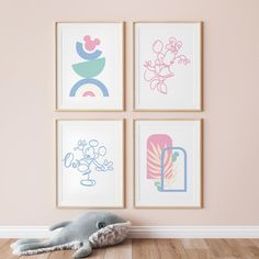 a stuffed animal laying on the floor in front of four framed art pieces with pink walls