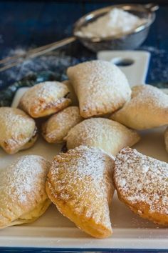 several pastries are arranged on a plate with powdered sugar and spoons in the background