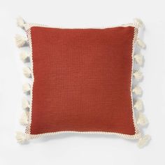 a red and white pillow with tassels on the edges, sitting on a white surface