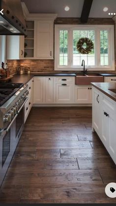 a large kitchen with white cabinets and wood flooring on the counter tops, along with a wreath hanging above the stove