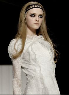 a woman with long blonde hair wearing a white dress and black headband on the runway