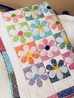 a colorful quilt is laying on top of a white bed sheet with flower appliques